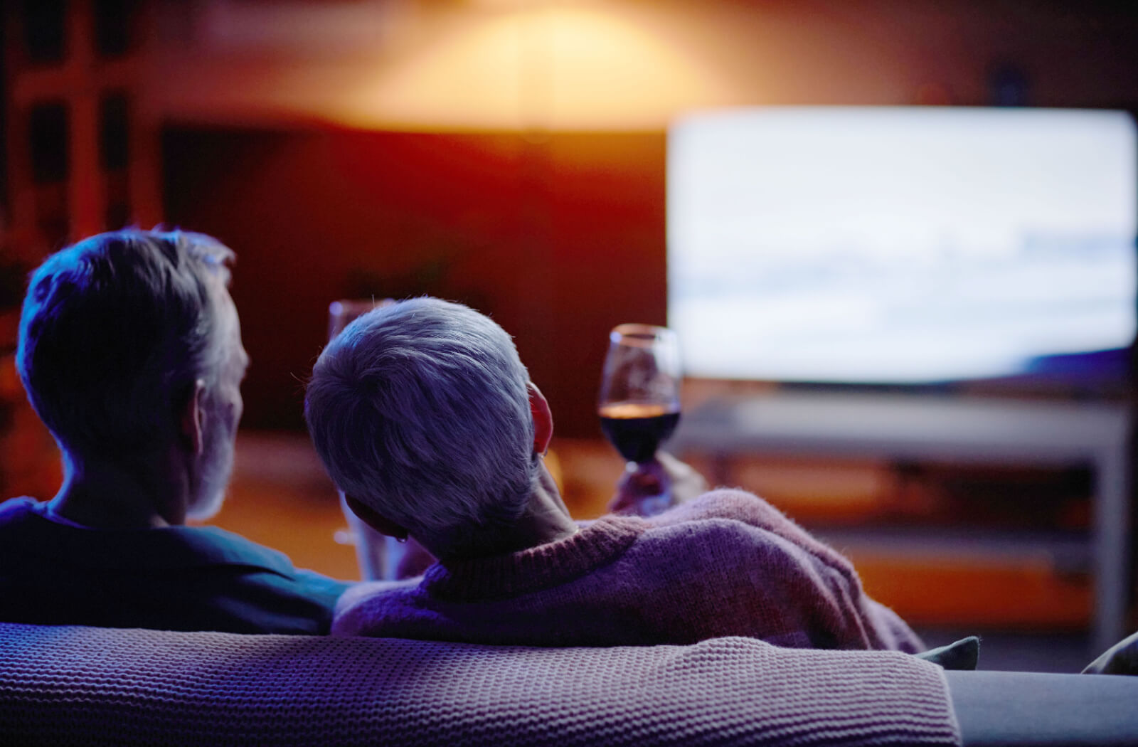 A shot from behind of an older couple holding glasses of wine preparing to watch a movie about Alzheimer's disease.