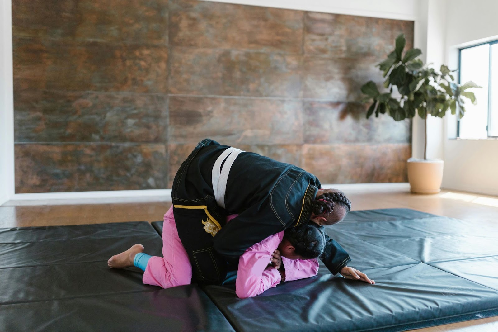 A martial arts instructor demonstrates grappling techniques to a young student in a training space.