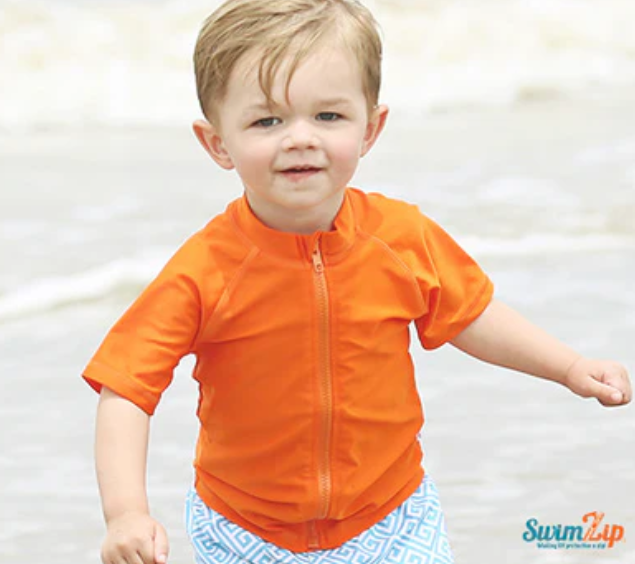 A boy running on the beach in a SwimZip's short-sleeved orange swim shirt—Are orange swimsuits safe?