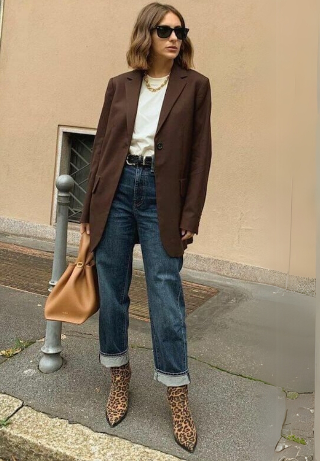 Wanita dengan jas coklat, celana denim, dan kaus putih.