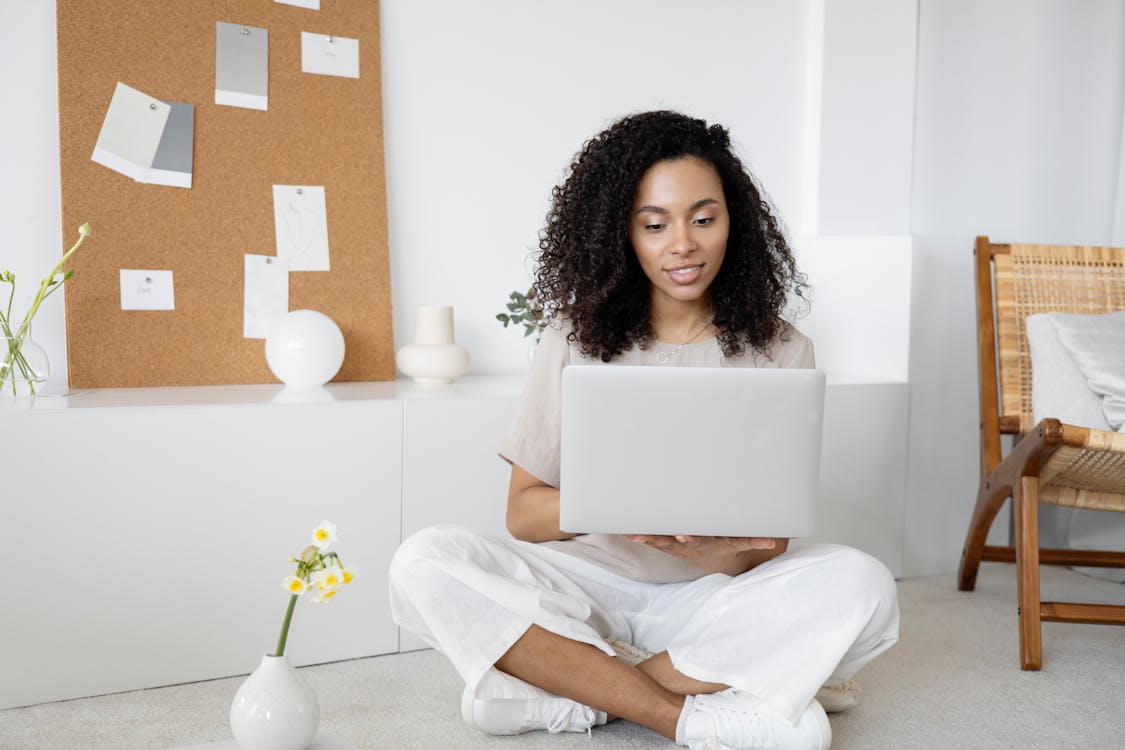 Free Young woman with curly hair working on her laptop in a cozy home setting, exuding confidence and focus. Stock Photo