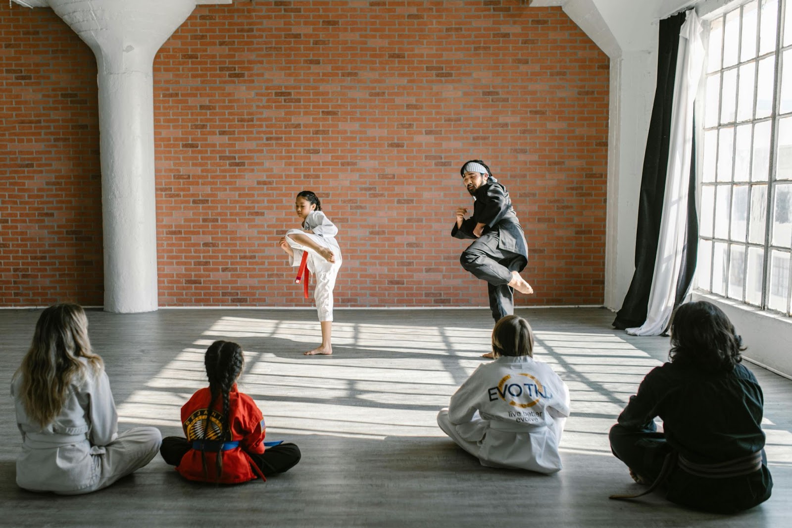 A martial arts instructor teaches a young student how to kick infront of a group of other students