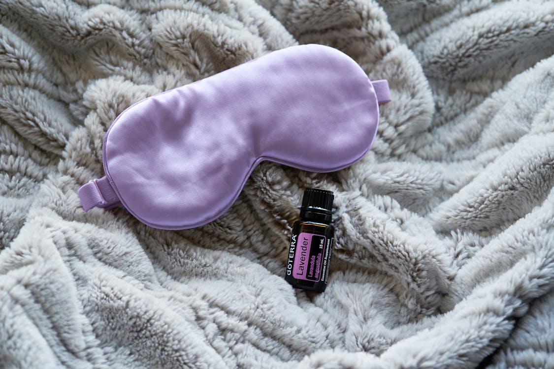 Free Lavender essential oil alongside a purple sleep mask on a gray blanket promotes relaxation and rest. Stock Photo