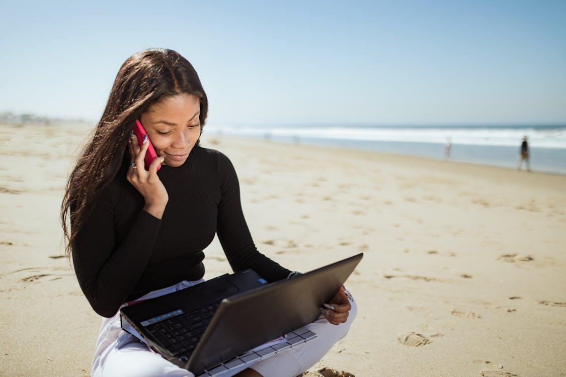 Free A Woman in Black Long Sleeve Shirt Using Laptop Computer on Beach Stock Photo