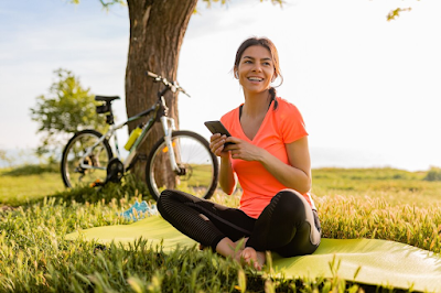 A woman seated beside her mountain bike, taking a break after a ride, with a serene landscape in the background.