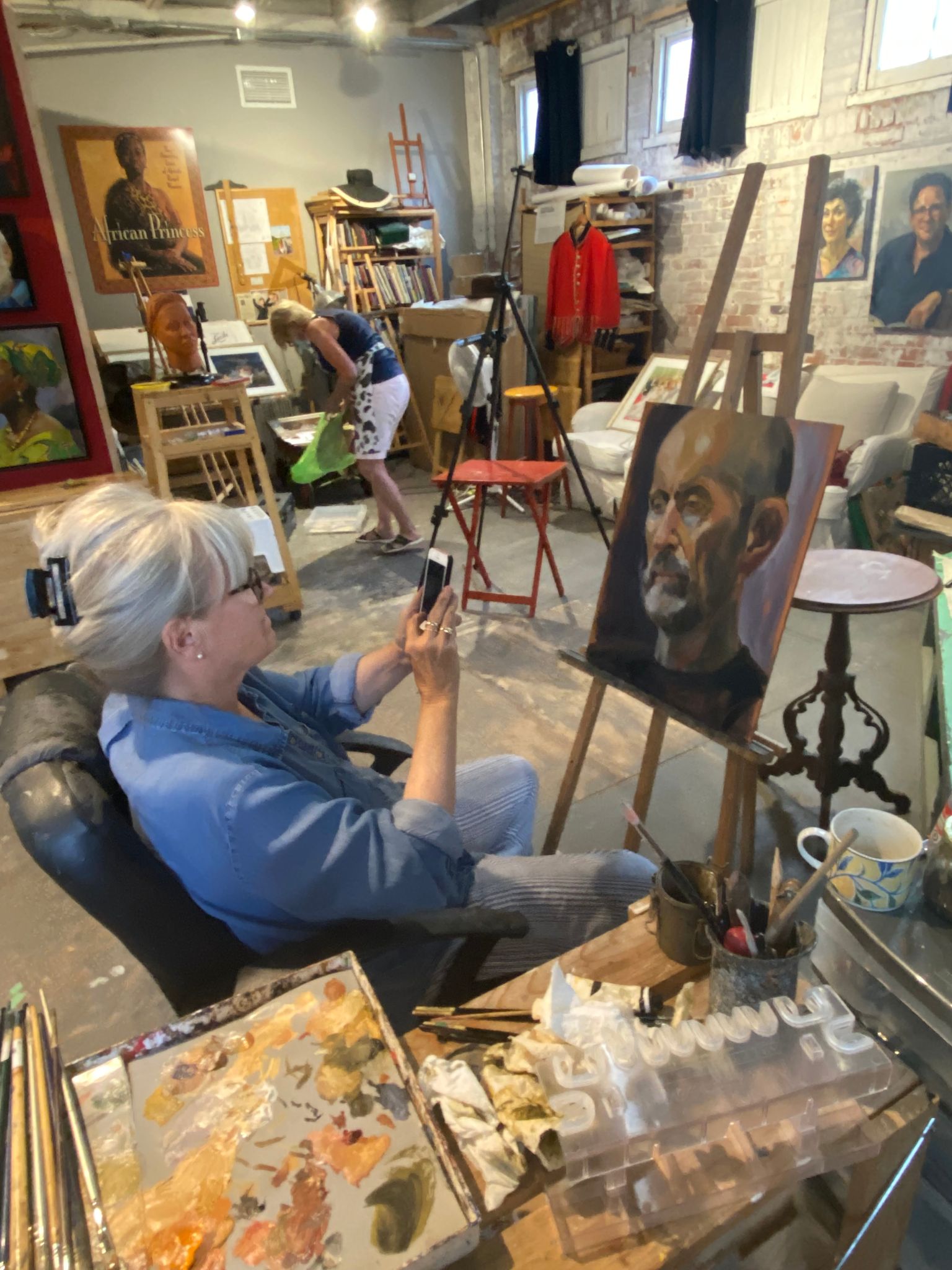 Woman in blue in an art studio taking a picture of a canvas