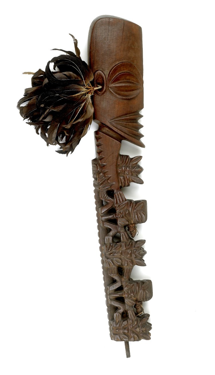 Sculpture. A long, carved, wooden sculpture depicts the profile of an abstracted human face, atop a decorated staff.
This large, wooden sculpture shows a stylized, human profile with its exaggerated eyes in a nearly-shut position, it's mouth calmly shut. Below the head are seven geometric figures protruding from a long staff. Thought they are sharply geometric, they seem to suggest human shapes. All are intricately carved and unique.

