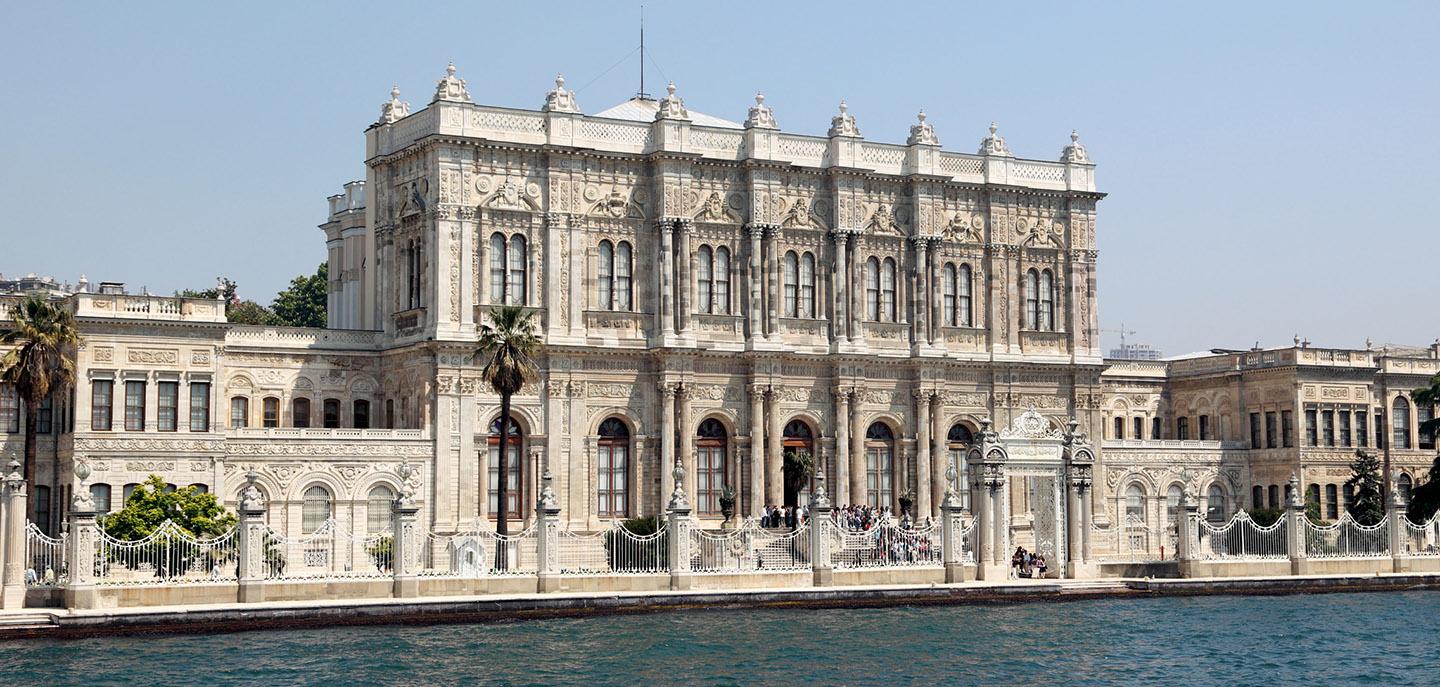 A large building with many windows with Dolmabahçe Palace in the background<br /><br />Description automatically generated