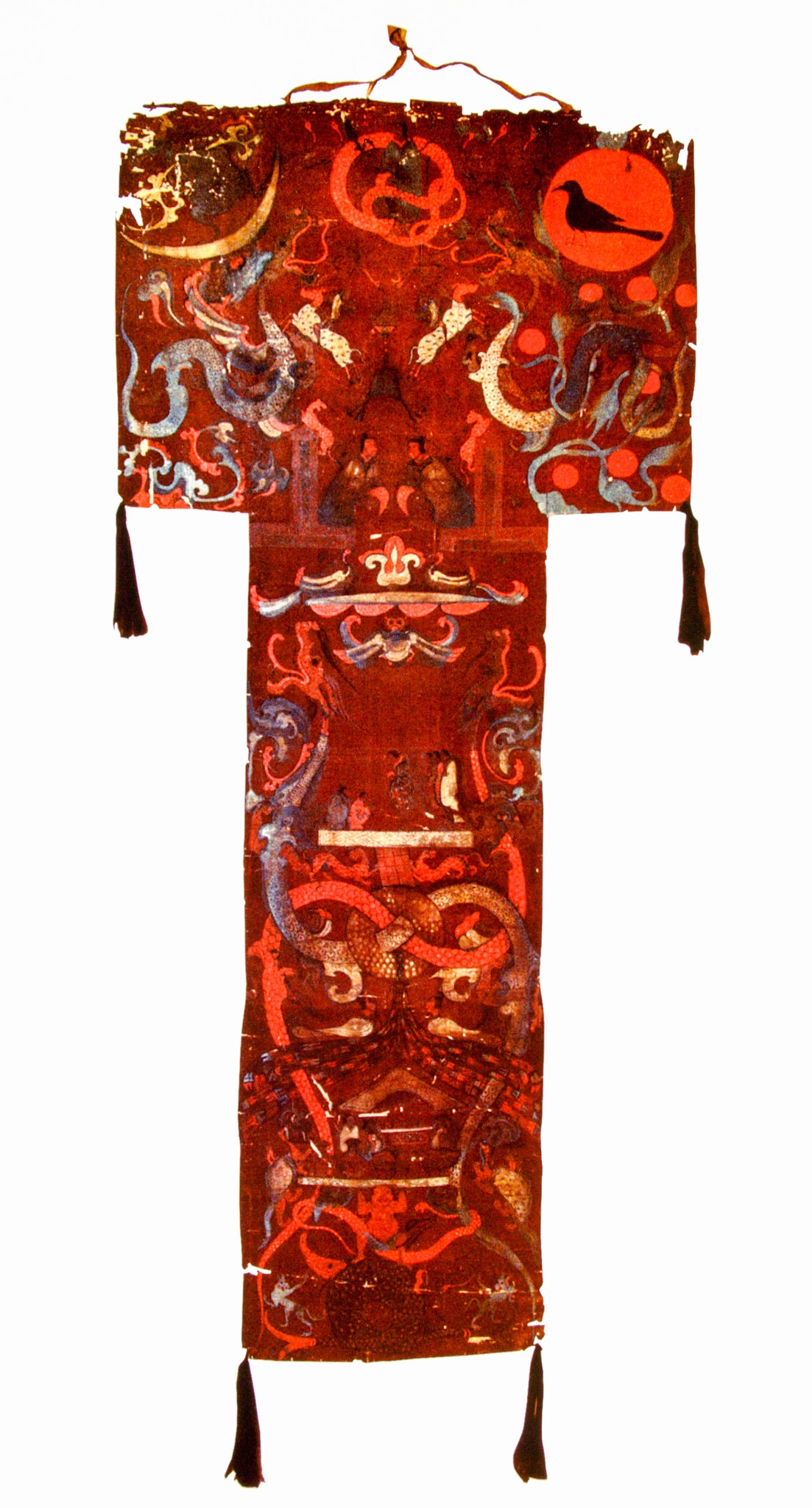 extile. A T-shaped painted cloth shows serpentine forms, scrolling leaves, people, and animals.
The piece across the top is only slightly wider than the long piece below. Tassels hang from the lower corners. The animals and decorations are painted in tones of deep burgundy and vivid red, gold, and pewter gray. A gold sliver of a crescent moon is in the top left, and a red disk with the black silhouette of a bird to the upper right.
