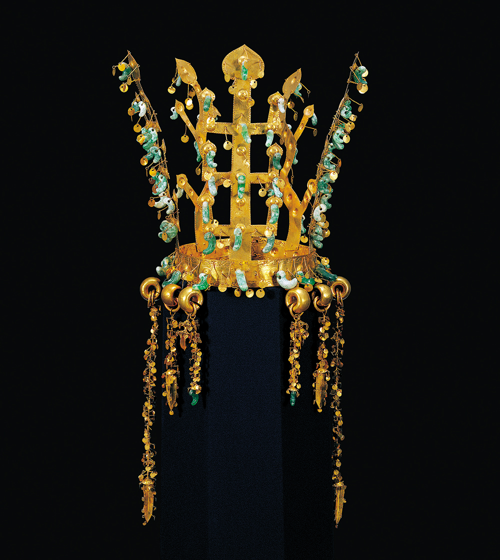 Jewelry. Crown-shaped piece with geometric lines and antler-like forms made with gold and jade.
This piece has an elaborate base structure in gold metal, with five separate spikes reaching upwards and six separate linked chains dangling gracefully from the main circlet. Dozens of small, carved comma-shaped jade pieces adorn the spikes and the delicate chains.

