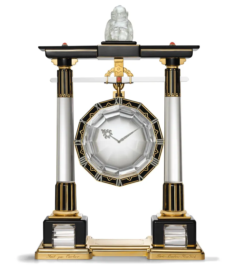 Cartier 'Portico' mystery clock: a central twelve sided disc of rock crystal with a black enamel border set with gold numbers. The clock hands appear to float on the surface. The disc is suspended from a framework shaped like the portico of a Japanese shrine, with a pillar of rock crystal with black and gold details on each side. Above the upper beam, a small carved rock crystal figure is seated. 