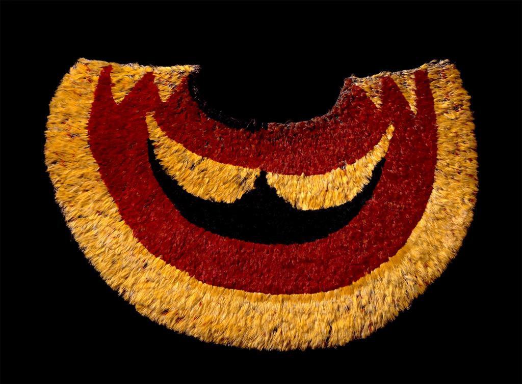 Garment. This feather cape is semi-circular in shape, with a solid pattern of broad swathes of deep red and gold.
The outermost edge of the cape is a deep gold, followed by a red semi-circle within, and then two more slightly-broken patterns in gold and then the innermost layer in red.

