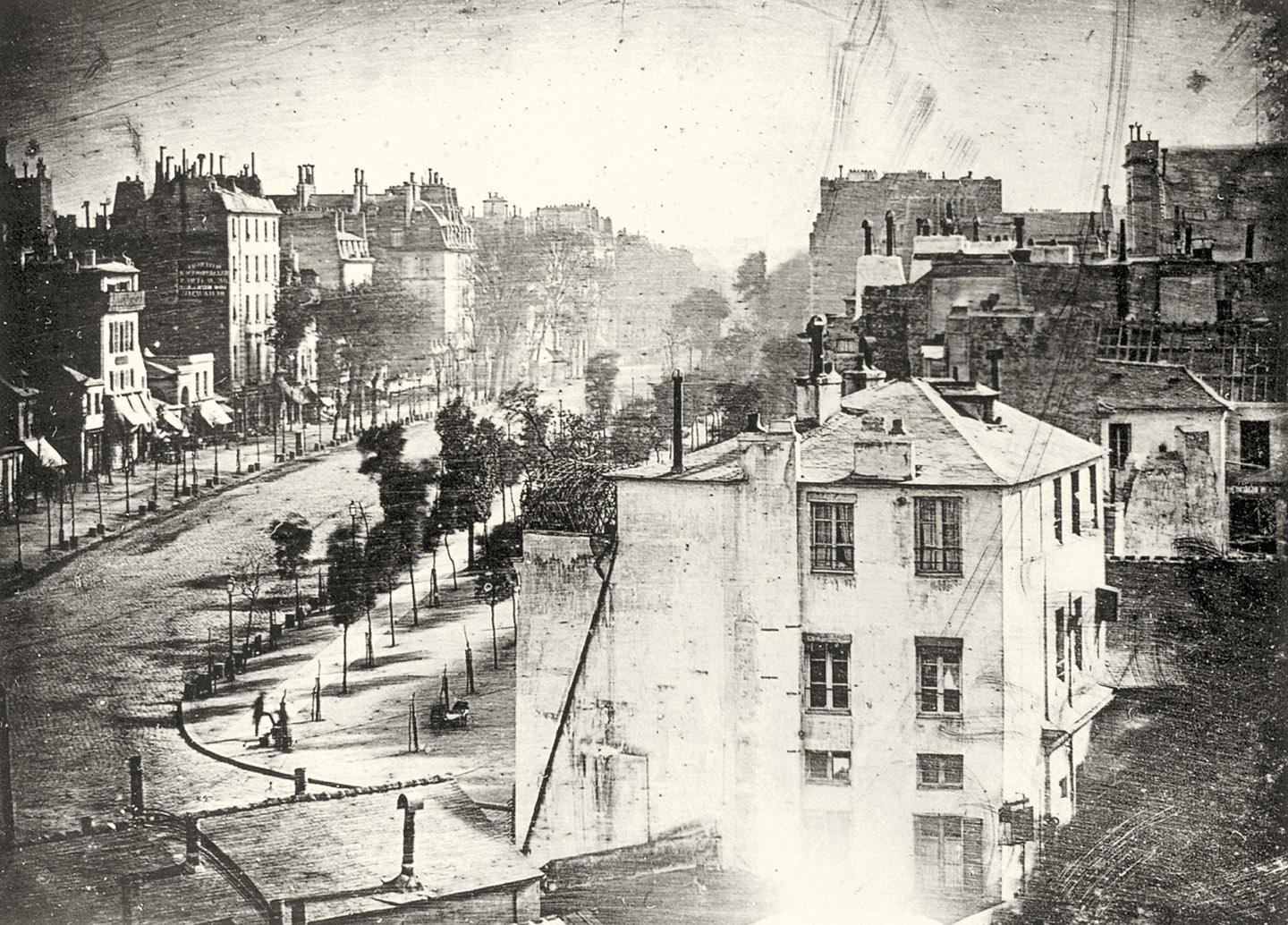 A black and white photo of a street with buildings<br /><br />Description automatically generated