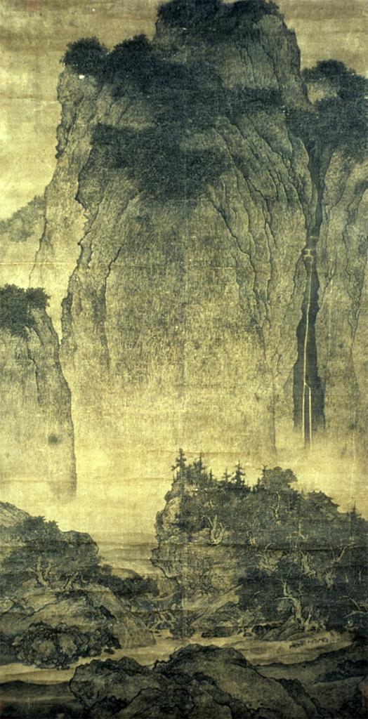 Painting. In ghostly and slate grays against golden-tan silk, a mountain cliff rises majestically over a walking path.
The sheer cliff takes up the top two-thirds of the tall scroll painting. The tops of the cliffs are dusted with darker vegetation. A break in the stone could be a waterfall to our right. The cliffs fade near their base, so spiky trees lining rocky banks below are outlined in stark silhouette against the golden background. A boulder along and nearly spanning the lower edge is between us and the walking path there. Barely visible in this image, two miniscule people and three donkeys walk along the path to our right.

