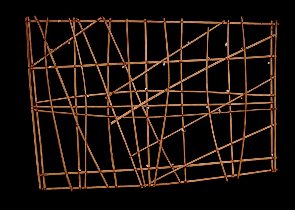 Sculpture. Sticks arranged in a grid, and lines that cross over the grid, create a chart-like structure.
This grid made of sticks as representative lines has a rectangular frame, and eleven horizontal lines going across this frame. We also see one diagonal line crossing from the upper left to the lower right corner of the rectangle. Three slightly-curved lines are in the middle, vertically oriented, and one odd, pentagonal shape juts out of the bottom left corner. The background of this image is blue, the lines/sticks are all light brown.

