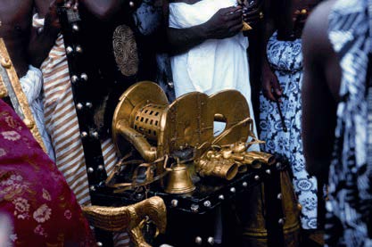Sculpture. Heavy, gold sculpture of a stool, but light enough for humans to carry, with bells and other accoutrements.
This gold sculpture is complex and surrounded by people who regard it reverently as it rests on a decorated table.

