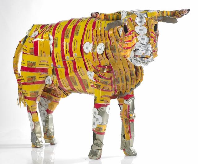 Sculpture. Mixed media, combining various commercial items, construct the shape of a cow in garish, unrealistic colors.
This multimedia sculpture of a cow is made of repurposed materials, as evidenced by the writing, logos, and labels that are visible in repetitive patterns across its entire body. The colors include a dominant gold, as well as red, white, black, and silver. These materials cover the surface of a representation of a cow, standing in a docile position. Its head is lowered, its gaze very gentle, staring straight at the viewer.

