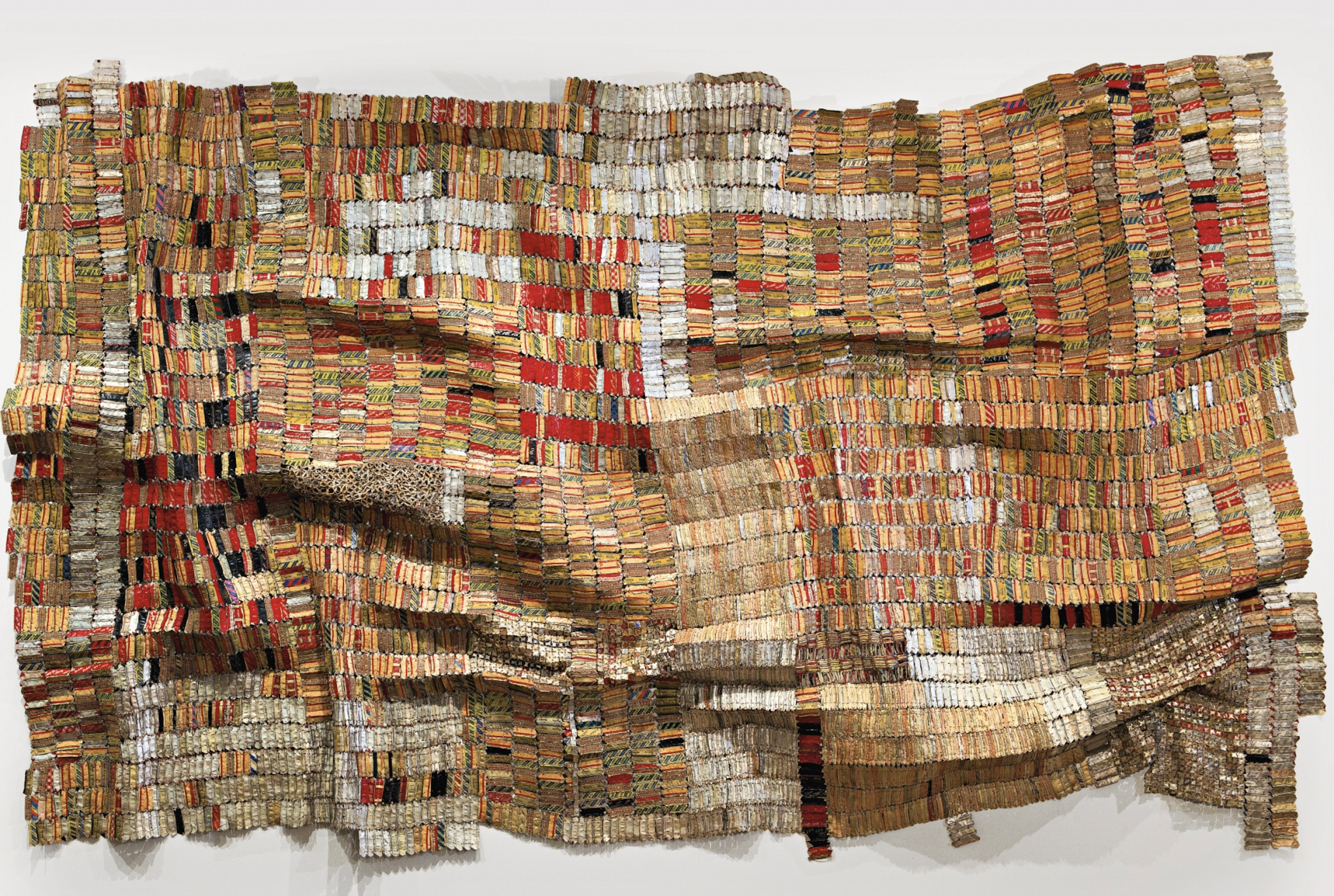 Sculpture. Multi-colored metal and copper wire are woven to resemble a large, wrinkled textile mounted on a wall.
The metal components of this sculpture are refined, detailed, and intricately-woven to the point that the surface looks like cloth hung on a wall. Golds and browns dominate the overall color palette, with reds, whites, and blacks weaving throughout, lending bright accents.

